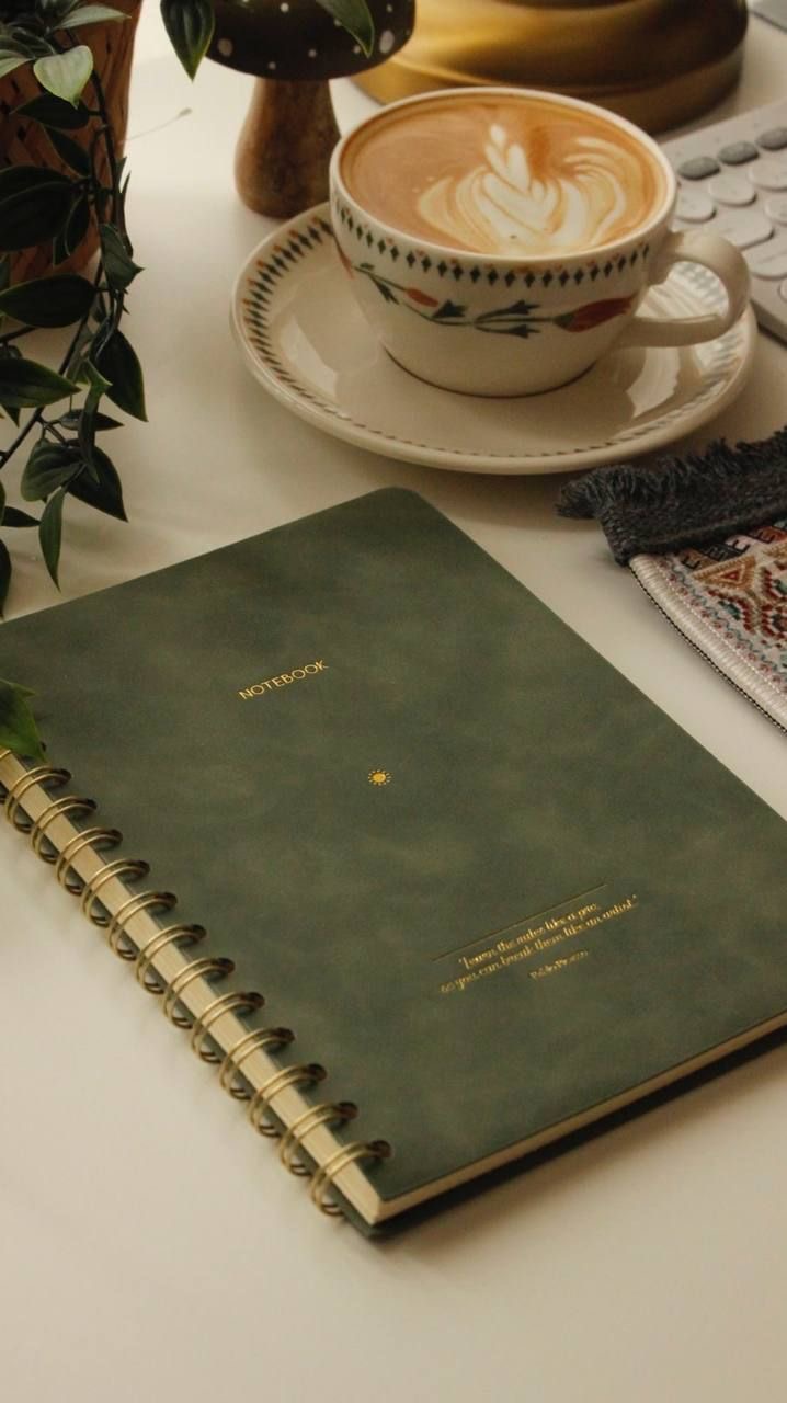 A green notebook, coffee and plant on a calm desk
